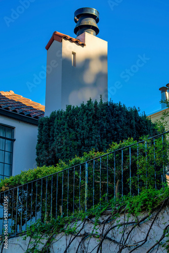 House or home with chimney sunspot metal vent with adobe red roof tiles and fence with vines shrubs and foliage photo