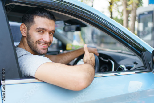 Happy cheerful Asian ale car driver waving or showing thumb up and smiling out of the car. Happy man waves a hand and smiles to camera close up with copyspace. Safety driving and insurance concept.