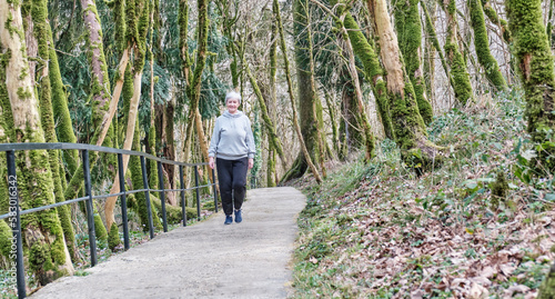 Senior woman walking along tourist trail in relic forest. photo