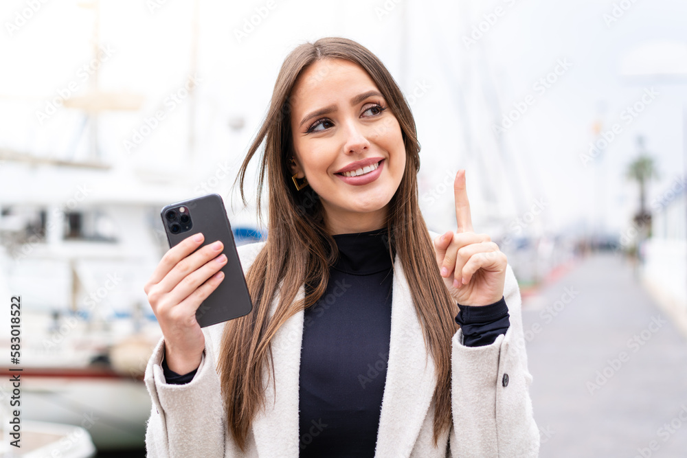 Young pretty woman using mobile phone at outdoors intending to realizes the solution while lifting a finger up Young pretty woman using mobile phone at outdoors intending to realizes the solution while lifting a finger up