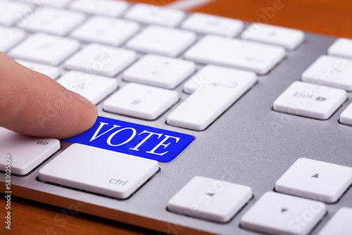 Finger pressing on vote blue button on keyboard. Online elections photo