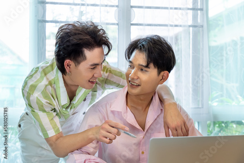 Cute Asian LGBT gay man couple, using laptop working at home, spend time together.