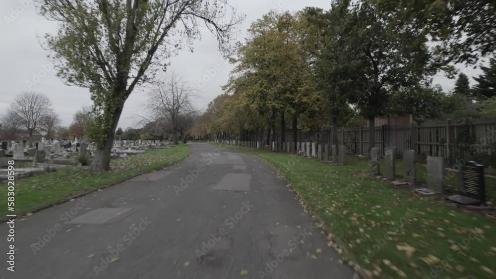 Road in city cemetery. Autumn leaves on grass between gravestones. Forwards fly above path. London, UK Road in city cemetery. Autumn leaves on grass between gravestones. Forwards fly above path. London, UK
