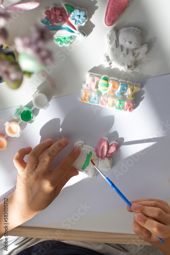 A child paints an Easter bunny figurine. Easter children's crafts.