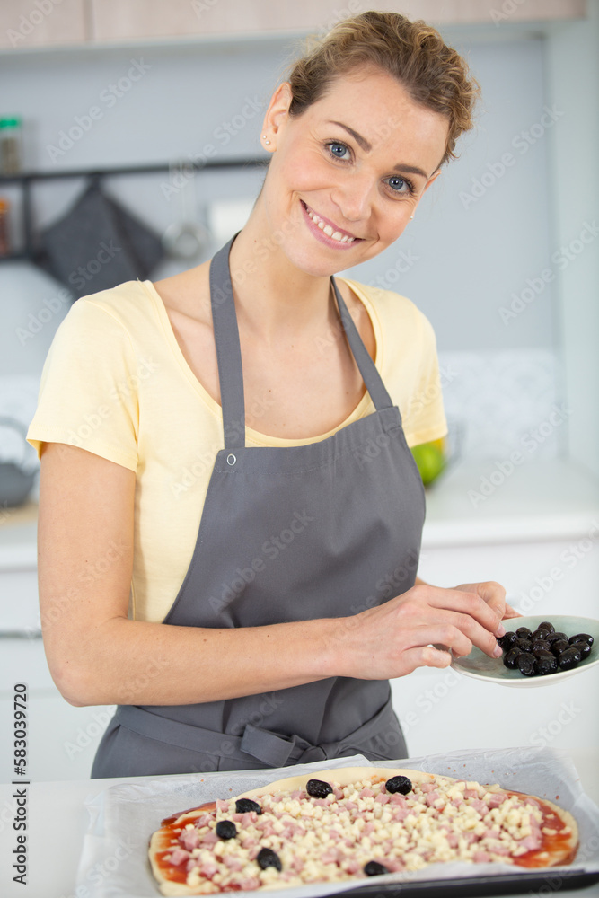 woman adding olives to a home made pizza