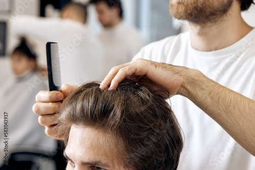close-up, professional male hairstylist combing young customer's hair