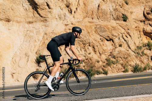 Cyclist in black sportswear doing intense training outdoors. Side view of a triathlete on a bicycle.