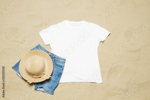 Sand beach texture background. Mockup white summer t-shirt outfit copy space. Blank template woman shirt Top view. Summertime accessories denim, bag. Flat-lay closeup tshirt on seashore. Beachtime