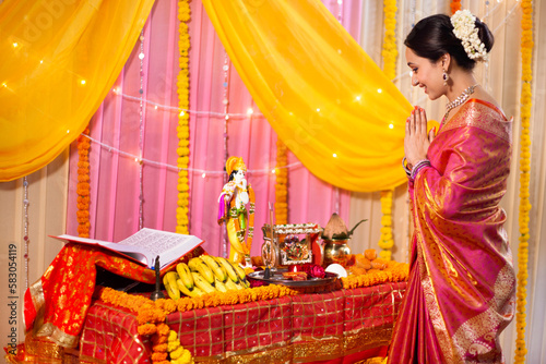 Indian  ethnic women worshiping supreme god Shyama - spiritual concept. Beautiful woman bowing head in front of Lord Krishna's idol 