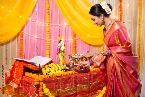 Indian woman wearing beautiful saree lighting Diya for 'aarti '. Young ethnic spiritual woman preparing Thaali of Aarti at home photo