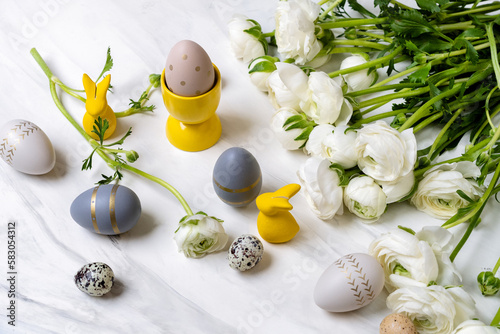 Easter eggs and Easter home decor yellow bunnies, white flowers ranunculus on a light background
