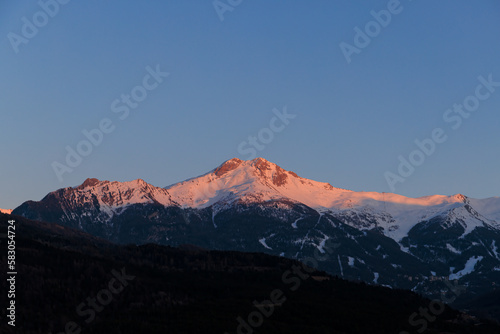 A scenic view of a majestic snowy mountain at dusk with sun ray at the top under a majestic blue sky 