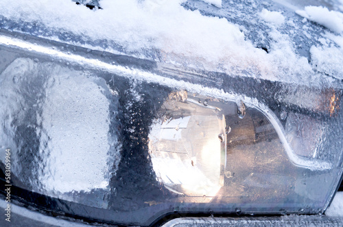 The headlight of a modern car is covered with ice.