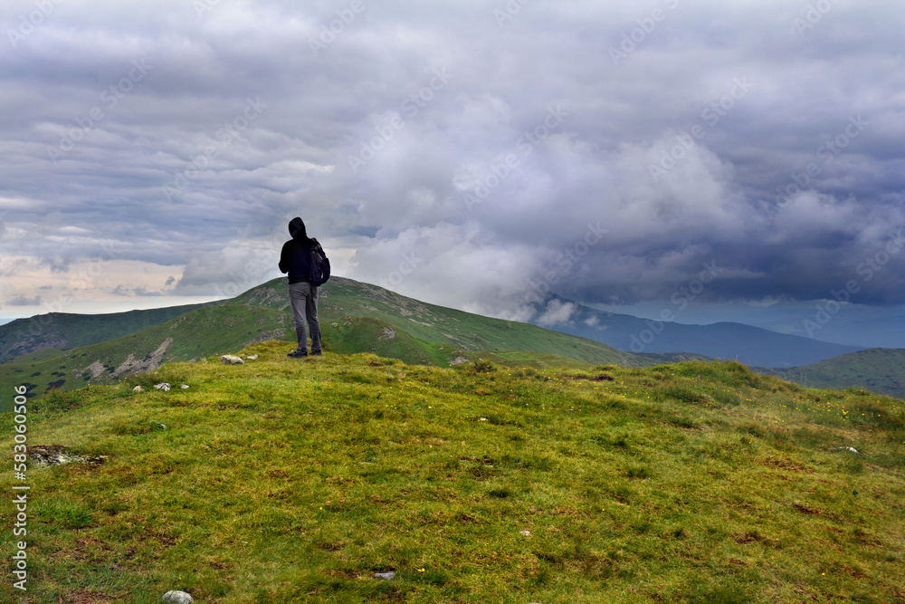Young hiker man standing on top of cliff on background mountain range of Chernogor in Ukraine. Thunderstorm dark clouds over Carpathian mountains landscape panorama