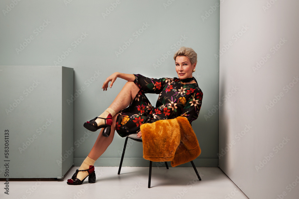Sexy mature woman fashion model sitting on chair in Studio wearing trendy  clothes, floral black dress with socks and mules sandals, looking camera  Stock Photo | Adobe Stock