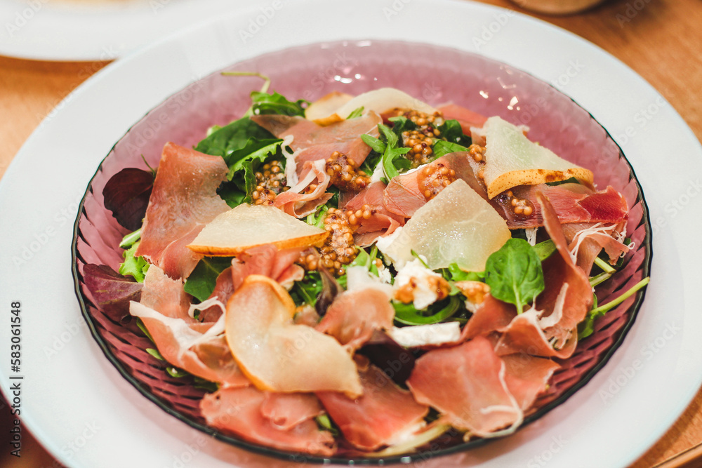 Salad with herbs, arugula, prosciutto, cheese, green olives and nuts.