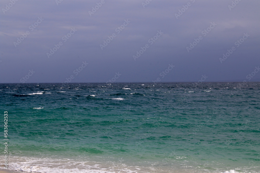 Seascape. Ocean is shaking. Small waves roll on the sandy beach in cloudy weather. Seascape. Ocean is shaking. Small waves roll on the sandy beach in cloudy weather.