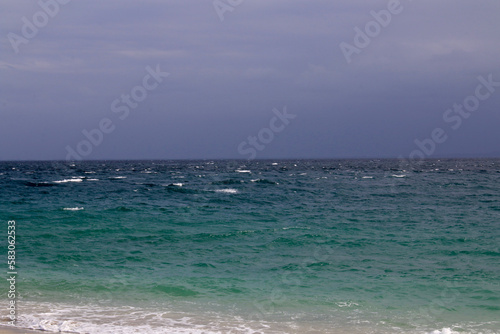 Seascape. Ocean is shaking. Small waves roll on the sandy beach in cloudy weather.