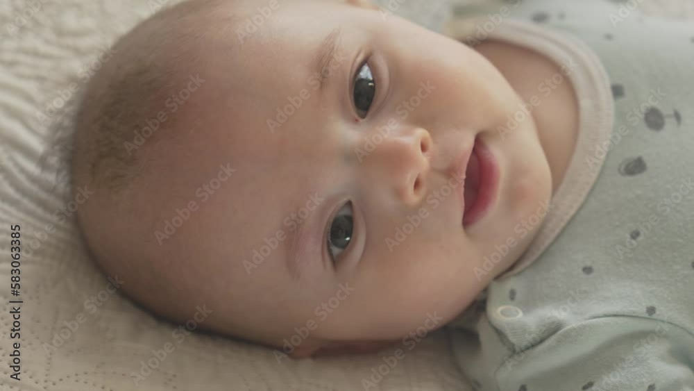 cute happy baby laying on his back in white bed sheets, looking with curiosity, portrait in bright bedroom cute happy baby laying on his back in white bed sheets, looking with curiosity, portrait in bright bedroom