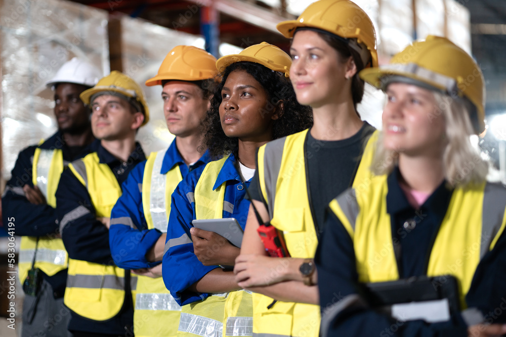 Multiracial group of men and women workers standing in merchandise storage warehouse in factory. Multiethnic people and colleagues working together, portrait. Diverse people teamwork. Selective focus Multiracial group of men and women workers standing in merchandise storage warehouse in factory. Multiethnic people and colleagues working together, portrait. Diverse people teamwork. Selective focus