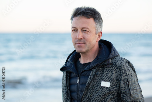 Handsome mature man at the beach, outdoor portrait. Attractive happy smiling adult male model posing at seaside, sunset or sunrise time