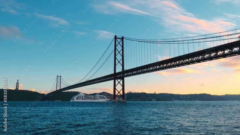 View of 25 de Abril Bridge famous tourist landmark of Lisbon connecting Lisboa to Almada on Setubal Peninsula over Tagus river with cruise liner passing under. Lisbon, Portugal