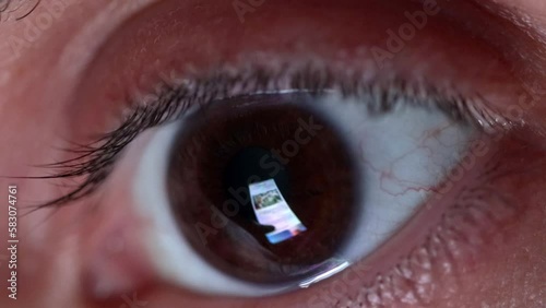 Detail of a man's eye looking at his smartphone screen while scrolling through online news and information. Online information and fake news, closeup macro detail of an eye. Scrolling smartphone feed
