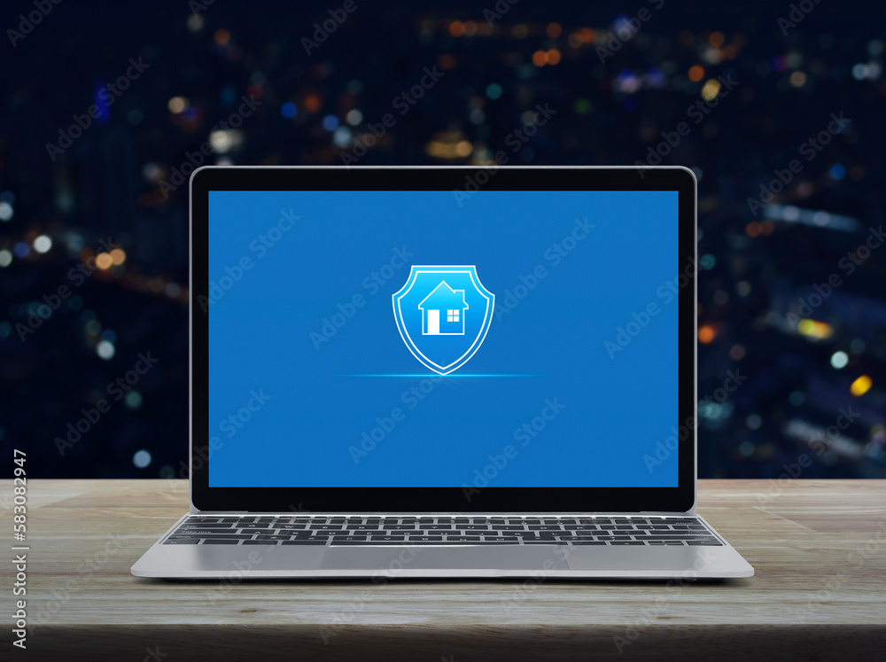 Home with shield flat icon on modern laptop computer monitor screen on wooden table over blur colorful night light city tower and skyscraper, Business home insurance and security online concept Home with shield flat icon on modern laptop computer monitor screen on wooden table over blur colorful night light city tower and skyscraper, Business home insurance and security online concept