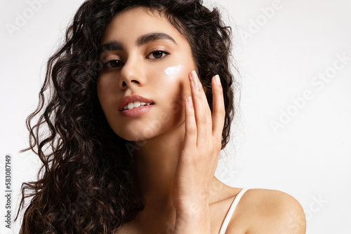 woman with natural make-up applying moisturizing facial cream. Girl with black curly hair