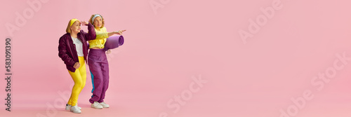 Looking with interest. Elderly sportive woman in colorful uniform posing with sport matt against pink background. Concept of sportive lifestyle, retirement, health care, wellness. Copy space for ad