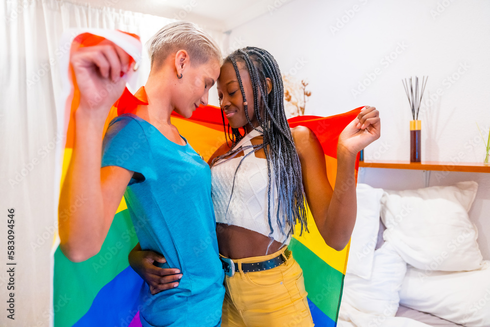 Beautiful lesbian couple kissing with rainbow flag indoors at home ...