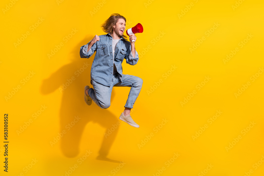 Full length photo of cheerful confident guy dressed jeans shirt jumping shout toa emtpy space isolated yellow color background