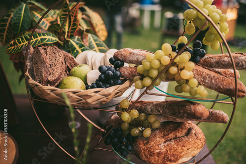 The board is set up on a long buffet table. The cheeses are arranged alongside sliced cured meats, fresh grapes, and berries, and the warm glow of the overhead lights adds to the overall ambiance 