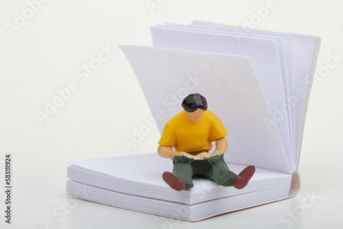 miniature figurine of a man reading inside a big paper book