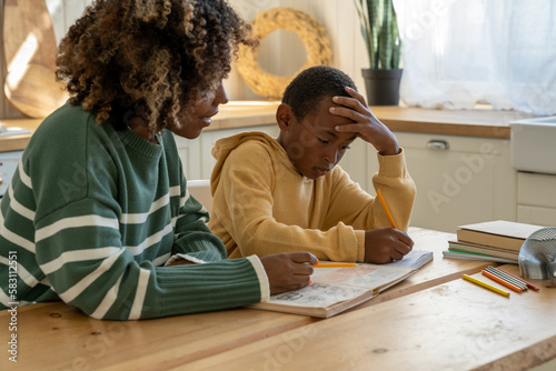 Homeschooling together. Caring African American mother helping thoughtful adopted son with tasks of school homework for effective education. Attentive private black tutor woman give lesson pensive boy