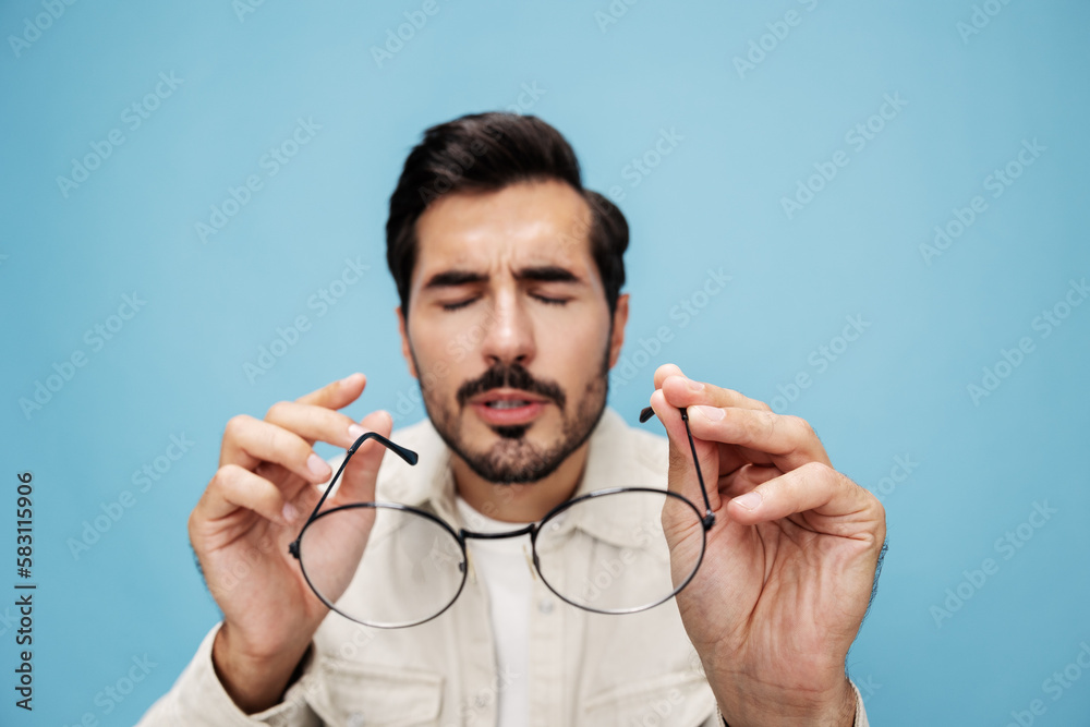 Close-up portrait of a brunette man looking through glasses, eye problems, eyeglasses for vision, on a blue background in a white T-shirt, copy space Close-up portrait of a brunette man looking through glasses, eye problems, eyeglasses for vision, on a blue background in a white T-shirt, copy space