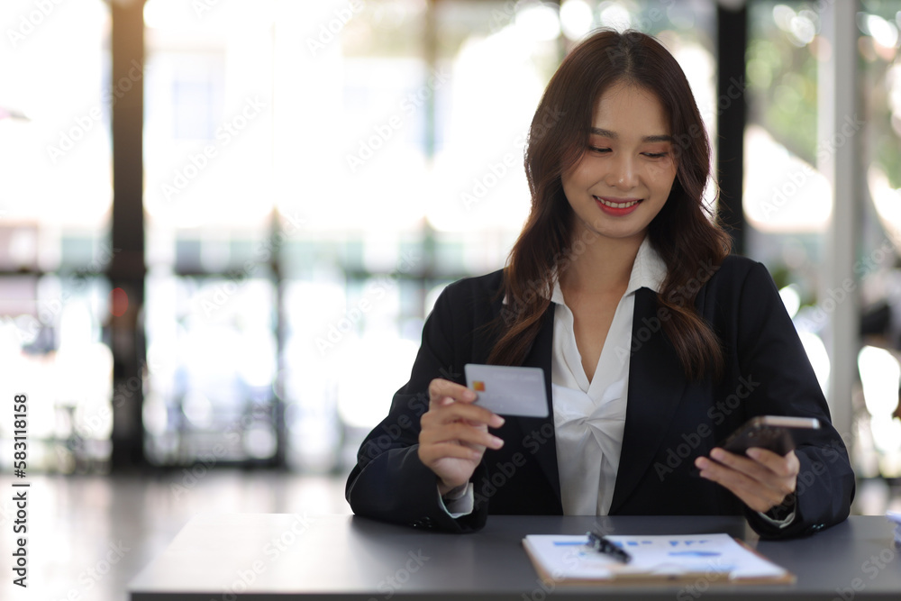 Businesswoman holding a credit card using a smartphone, Modern and convenient financial transaction concept. Businesswoman holding a credit card using a smartphone, Modern and convenient financial transaction concept.