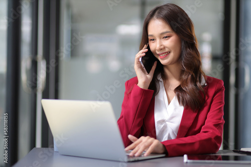 Beautiful Asian businesswoman talking on the phone with a customer while working at her desk in the office.