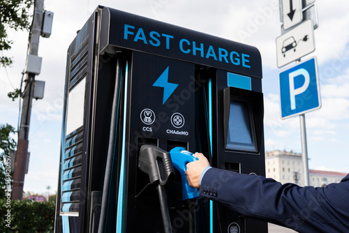 an electric car battery charging station on a city street. A modern gas station with electricity.. businessman charges an electric car