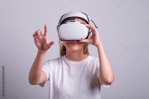 Surprised teen woman student use vr glasses and looks at empty space with gray background. Virtual gadgets for entertainment, work, free time and study. Virtual reality metaverse technology concept. © Bordinthorn