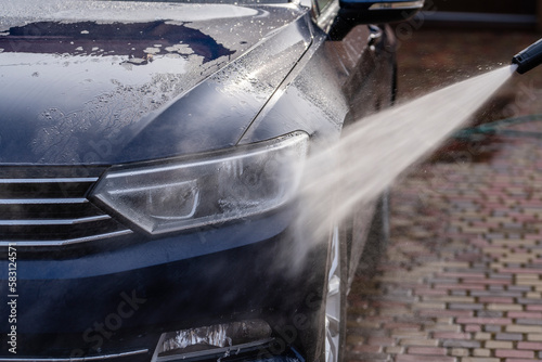 Washing a blue car with high pressure water cleaner, outdoors, closeup photo