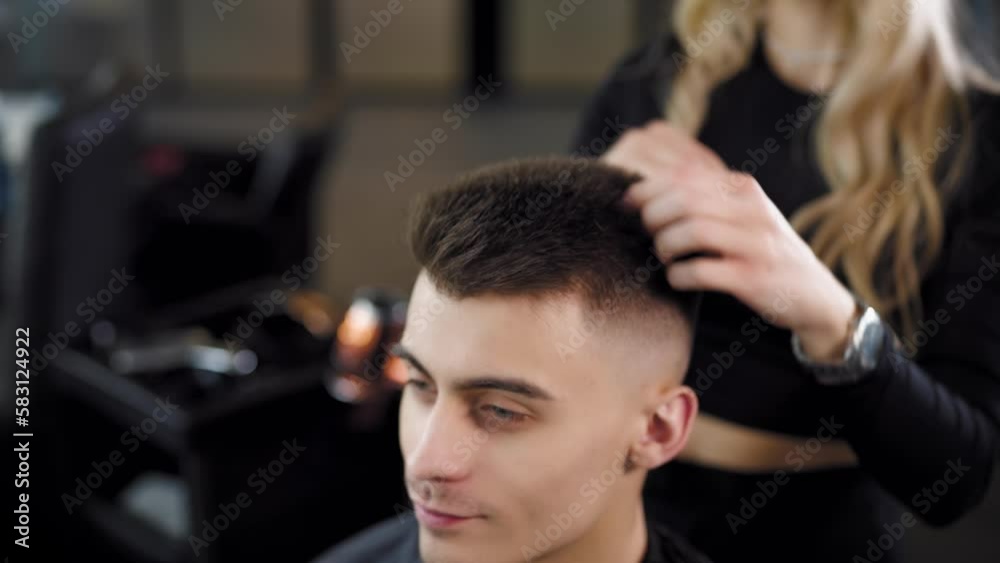A barber woman styling short hair with the hands of a young man in a barber shop. moving camera A barber woman styling short hair with the hands of a young man in a barber shop. moving camera