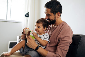 Father and baby son with teddy bear at home. Candid moment of father and son together.