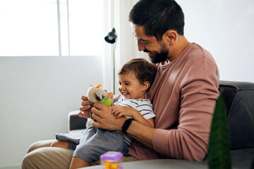 Father and baby son with teddy bear at home. Candid moment of father and son together.
