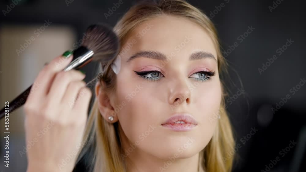 Close-up makeup artist applies powder to the face of a fashion model using a brush Close-up makeup artist applies powder to the face of a fashion model using a brush