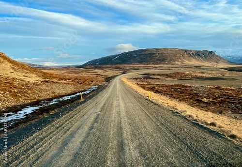 Piste de sable et de gravier traversant l'Islande et donnant sur une montage enneigée et parsemé de piquet jaune permettant de ne pas se perdre dans cette immensité 