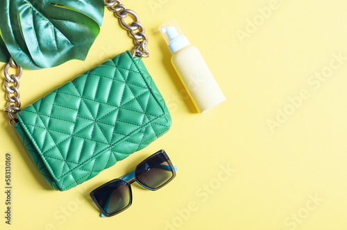 Stylish women's trendy green quilted bag with a large gold chain, cream in a bottle, sunglasses and a manster leaf photo