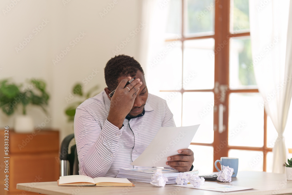 Tired American African business man in stress works with many paperwork document. migraine attack. Freelance, work from home Tired American African business man in stress works with many paperwork document. migraine attack. Freelance, work from home