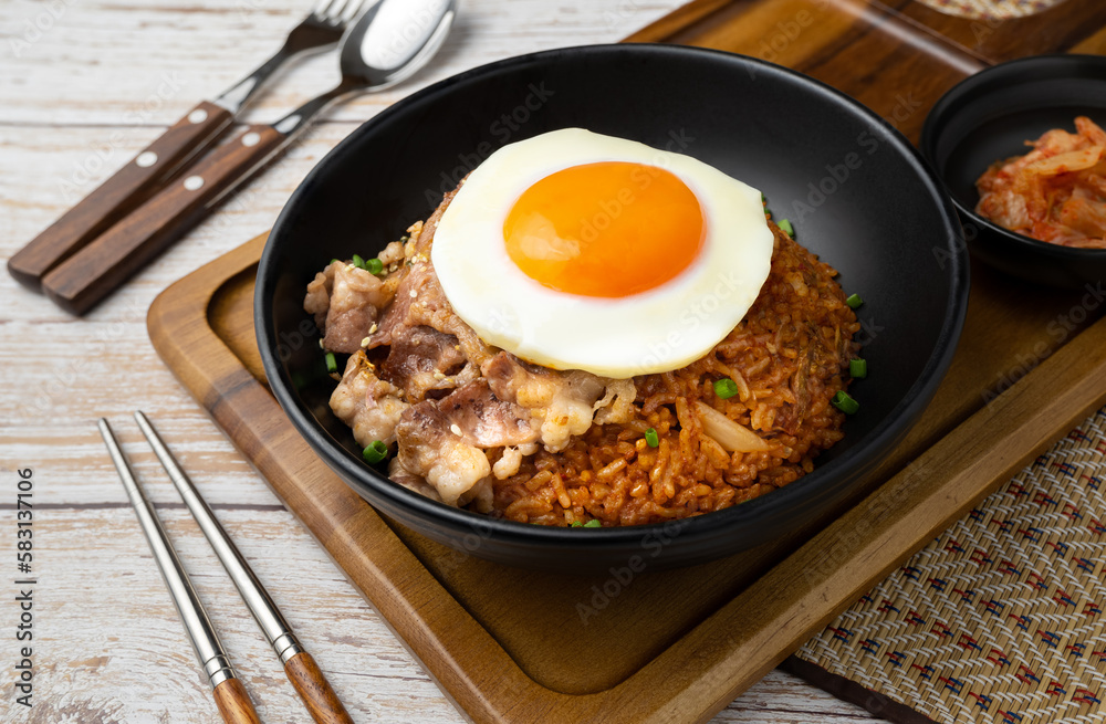 Closeup of Kimchi rice with grilled brisket sliced and fried egg in black bowl on wooden table. Closeup of Kimchi rice with grilled brisket sliced and fried egg in black bowl on wooden table.