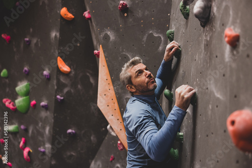 Mature male looking up with focus climbing a bouldering wall photo